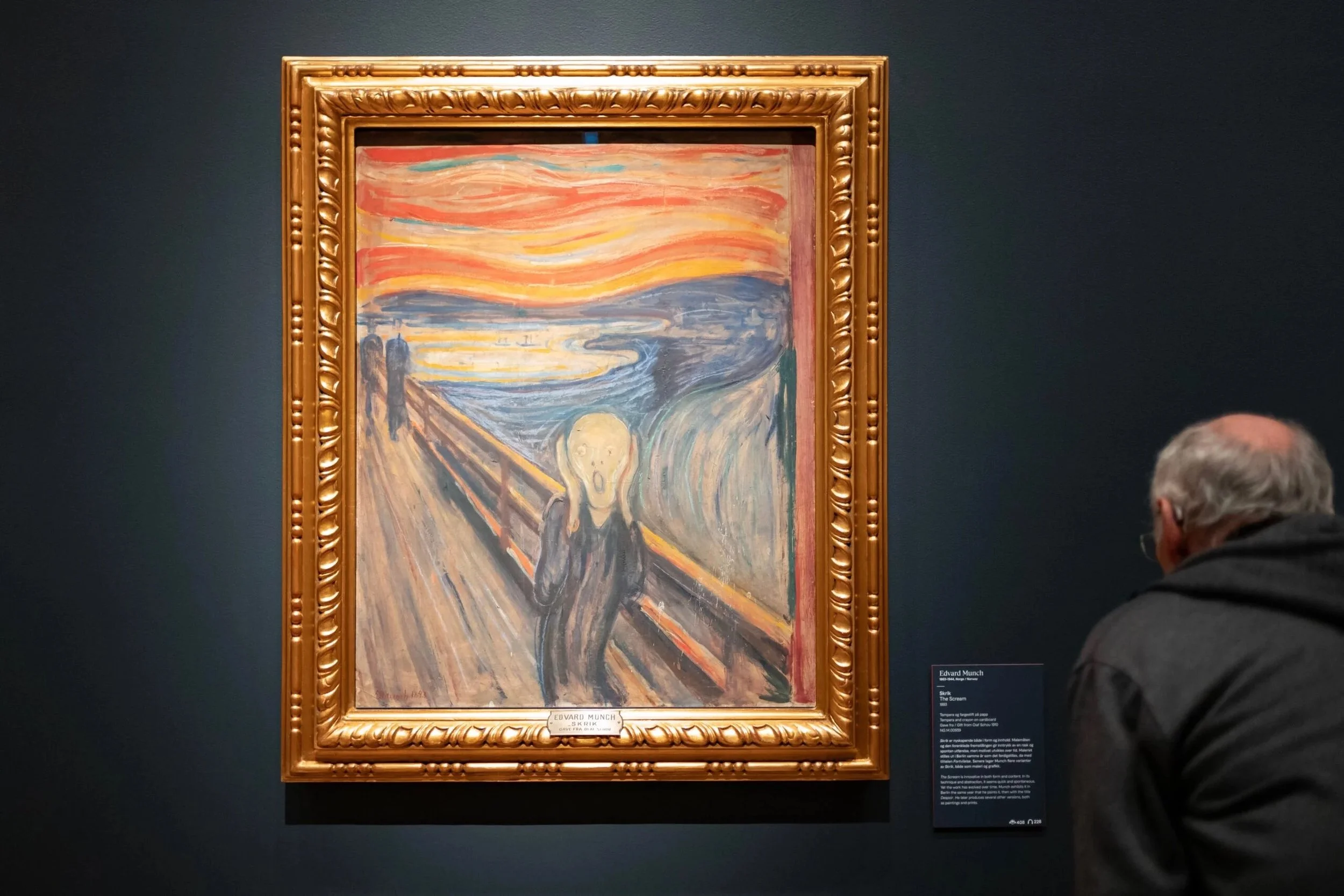 Peinture célèbre intitulée 'Le Cri' d'Edvard Munch exposée dans un musée, entourée d'un cadre orné, avec des visiteurs observant l'œuvre.