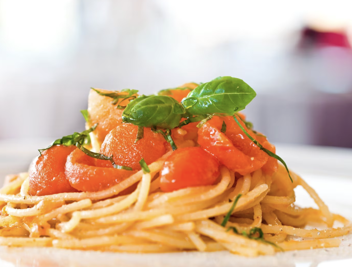 Just Travel met en avant un plat de spaghetti avec une sauce à la tomate, garni de basilic frais.