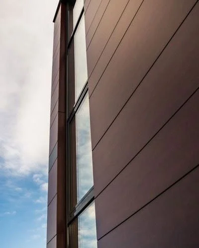 Close-up of a modern building's exterior wall with vertical windows reflecting the blue sky and clouds.