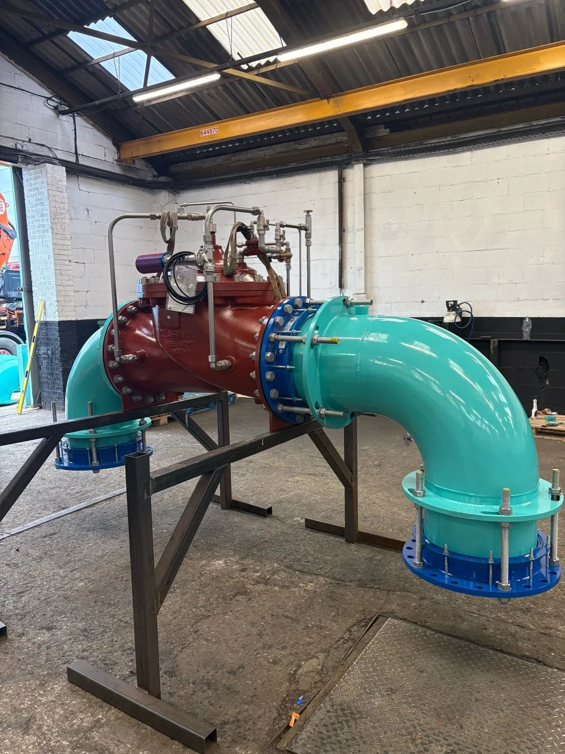 Large industrial pipe with red and turquoise sections inside a warehouse.