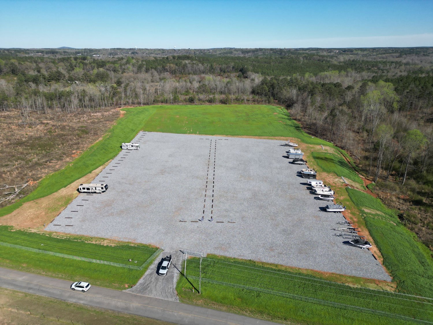 Empty gravel lot with parked RVs and trailers, surrounded by grassy areas and trees
