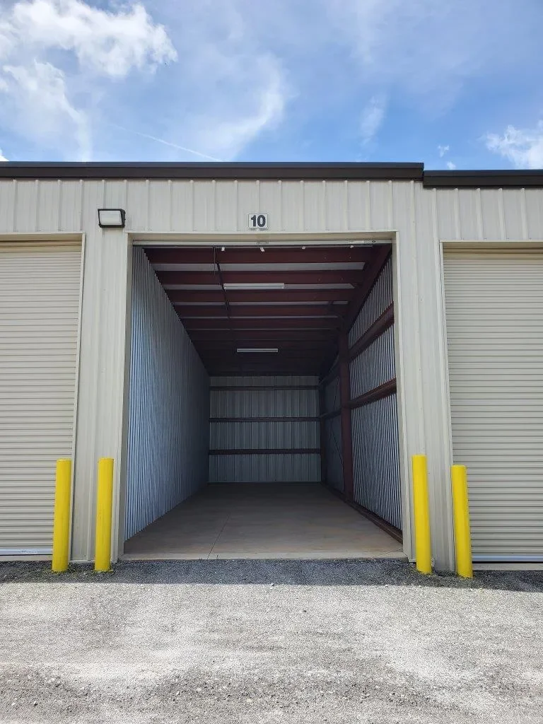 Empty storage unit with open door, metal siding, and yellow safety bollards outside