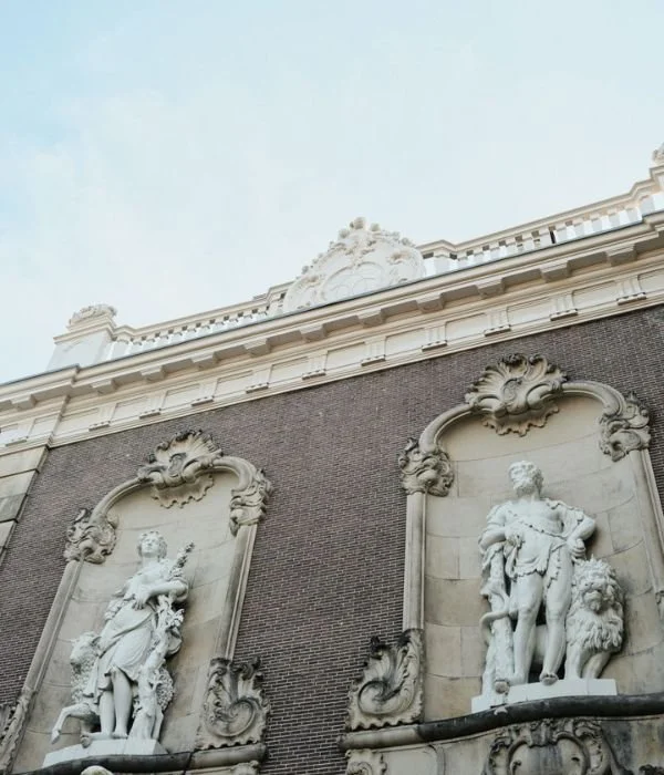 Close-up of historical building facade with two large stone statues of figures in armor, surrounded by ornate decorative framing, on a brick wall under a cloudy sky.