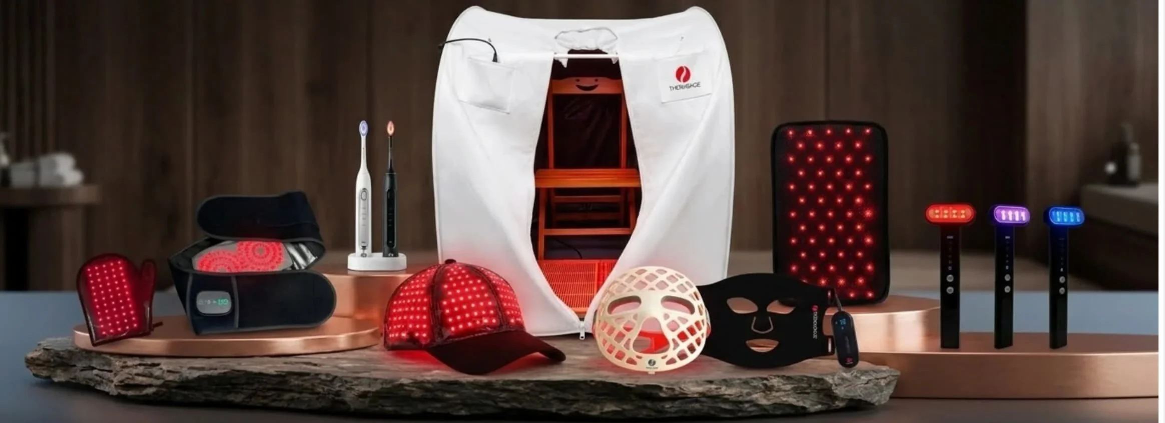 Collection of LED light therapy devices and accessories on a wooden surface, including masks, handheld devices, and a small tent for light therapy sessions.