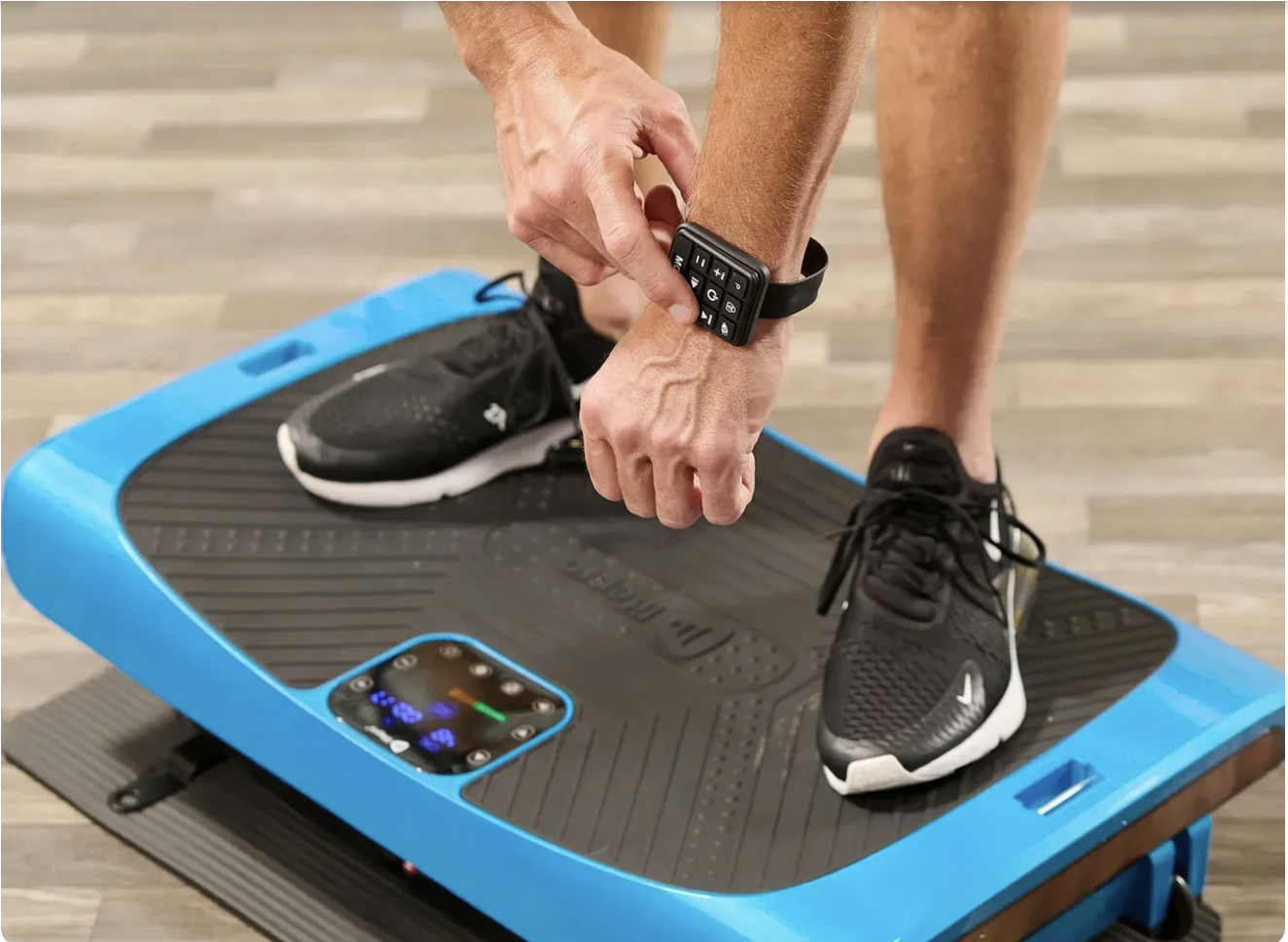 Person standing on a Lifepro mat, adjusting a device on their wrist, wearing black athletic shoes.
