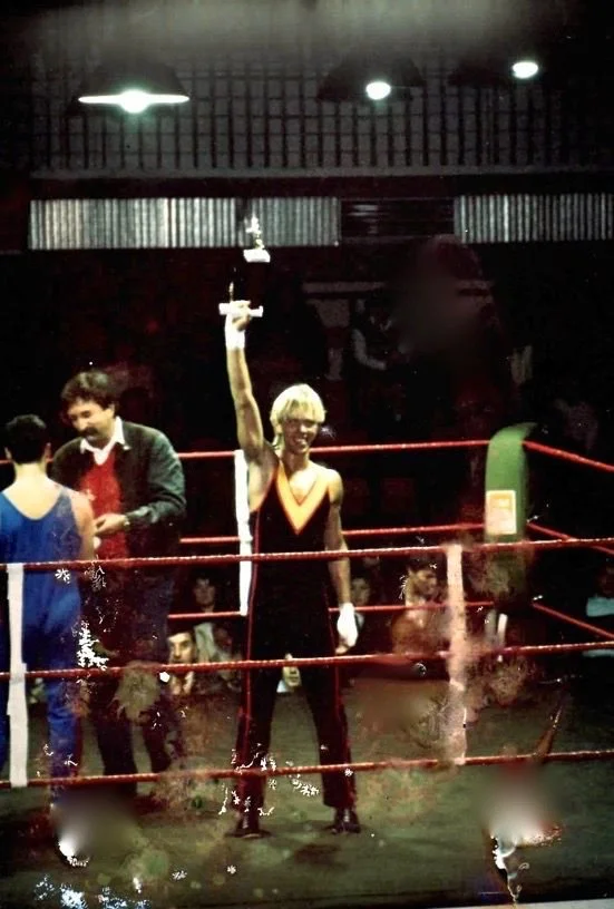 Une homme victorieux dans un ring de boxe, levant un trophée en l'air, entourée de personnes dans une ambiance de compétition