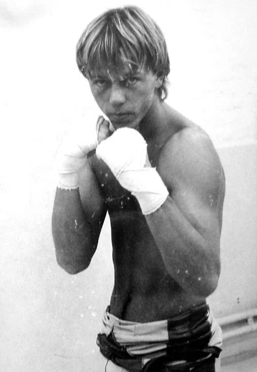 Un jeune boxeur dans une pose de combat, portant des bandes de boxe aux mains et des shorts de boxe, en salle d'entraînement.