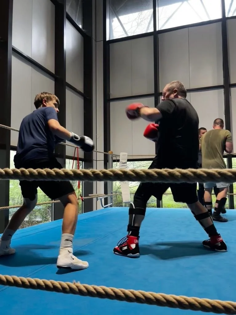 Deux hommes s'entraînent à la boxe dans un ring, face à face, avec des gants de boxe rouges.