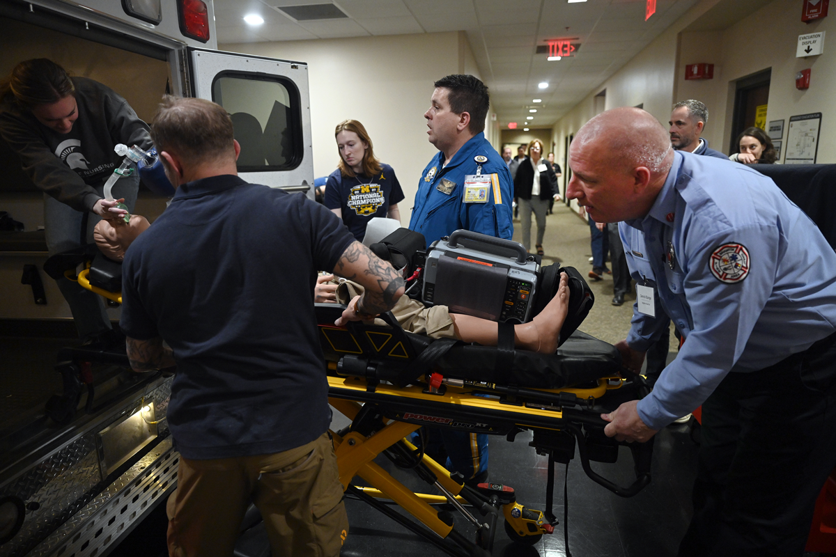 Workshop attendees load a medical manikin on a stretcher into the back of an ambulance.