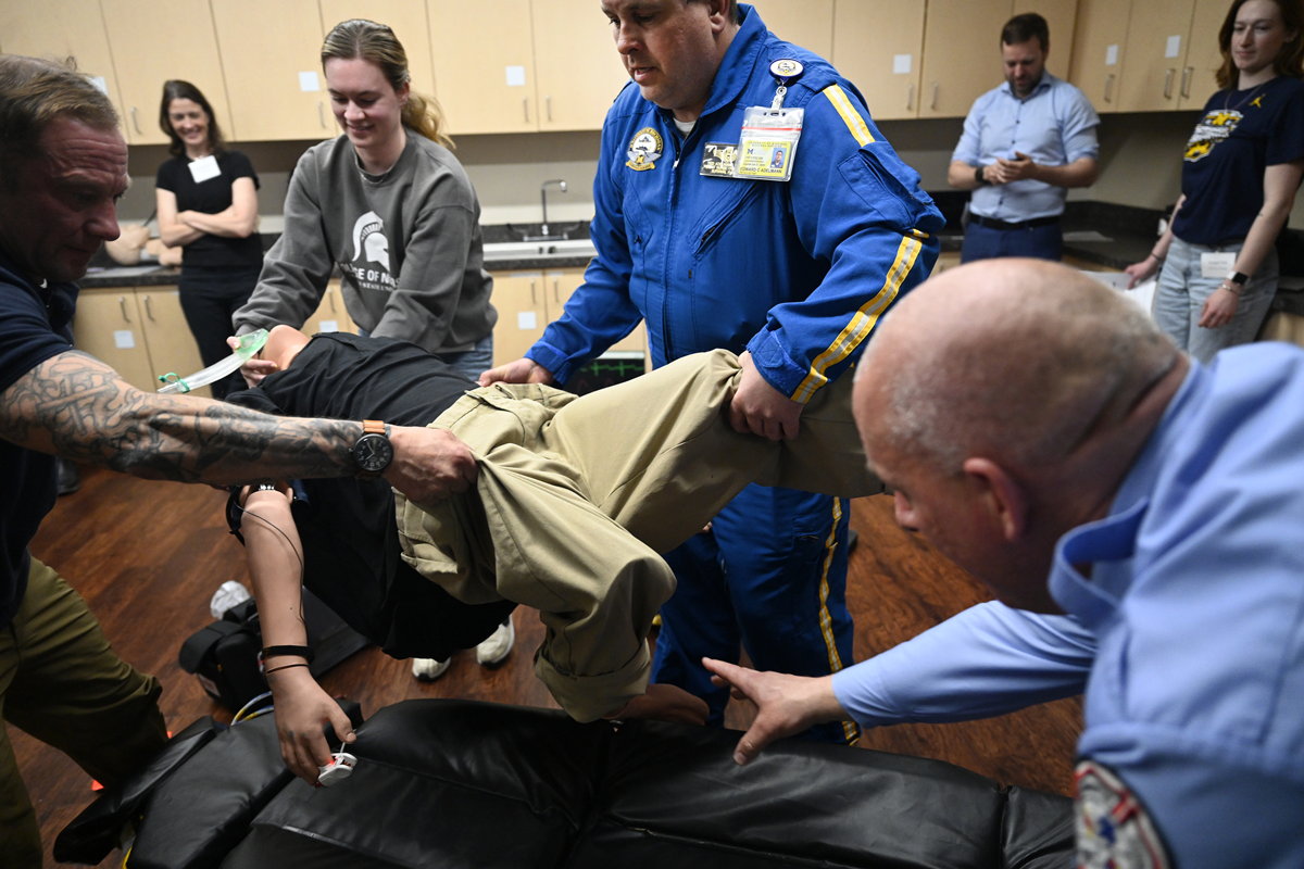 Workshop attendees work together to lift a medical mannikin from the ground and onto a stretcher, simulating moving a patient who has experienced an out-of-hospital cardiac arrest.