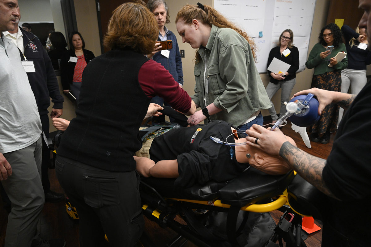 Workshop attendees transport a medical mannikin on a stretcher during a simulation of out-of-hospital cardiac arrest.