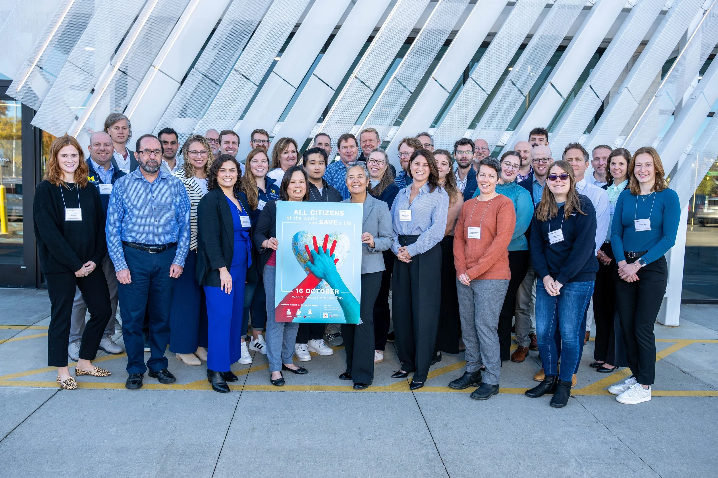 Members of the INSIGHT-CPR team pose outside of the venue of the 2025 INSIGHT-CPR team retreat and design-thinking workshop. In front, the team is holding a poster celebrating World Restart a Heart Day, which coincided with the retreat.