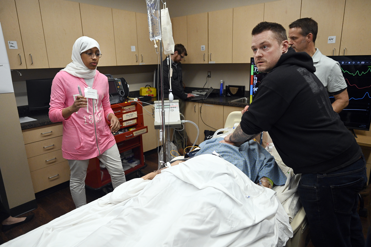 Workshop attendees perform CPR on a medical mannikin in a hospital bed as part of a simulation of in-hospital cardiac arrest.