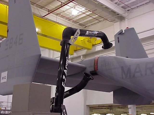Aircraft section being worked on in a hangar, with a black robotic arm fitted to the plane's fuselage, connecting to a yellow overhead crane.