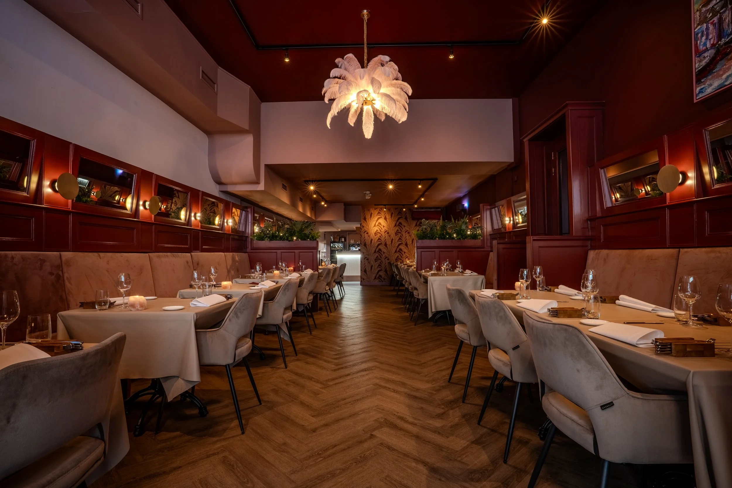 Een elegant restaurant in het centrum van Groningen met beige tafelkleden, gedekt met witte servetten en glaswerk, warme verlichting, roodbruine wanden en een opvallende witte pluimenvormige hanglamp in het midden.