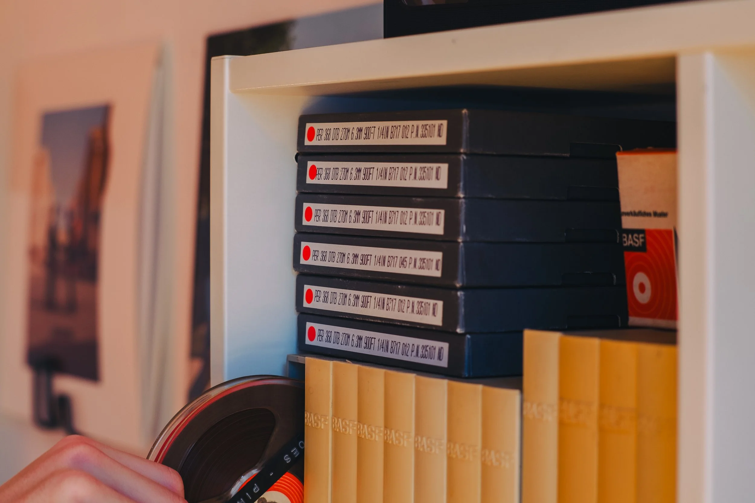 A person is pulling a vinyl record from a white shelf filled with black boxes labeled with white tags and red dots, with some yellow boxes on the lower shelf.