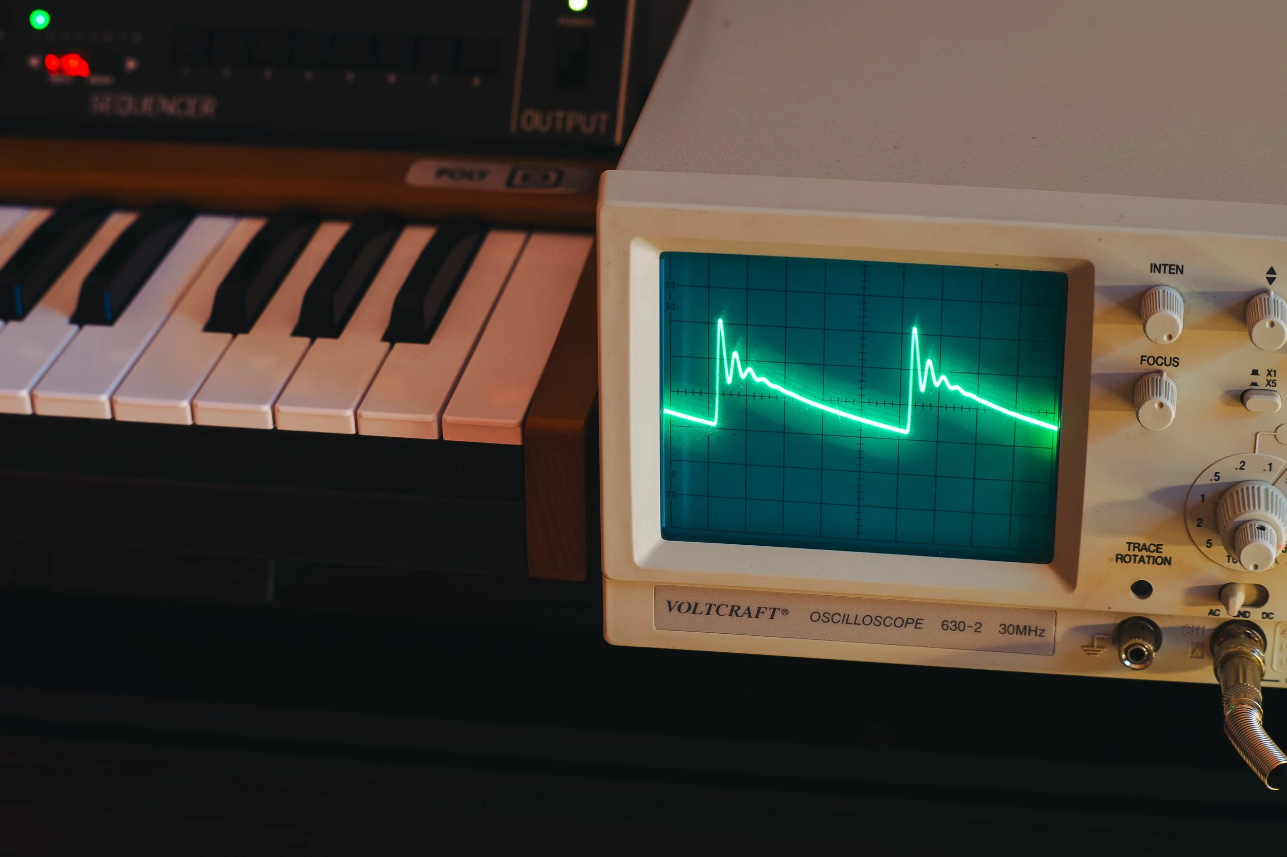 A partially visible keyboard with black and white keys next to a vintage oscilloscope showing a waveform display.