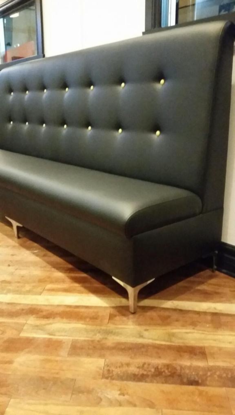 A black modern upholstered sofa with a tufted backrest, metal legs, and wooden flooring in a room.