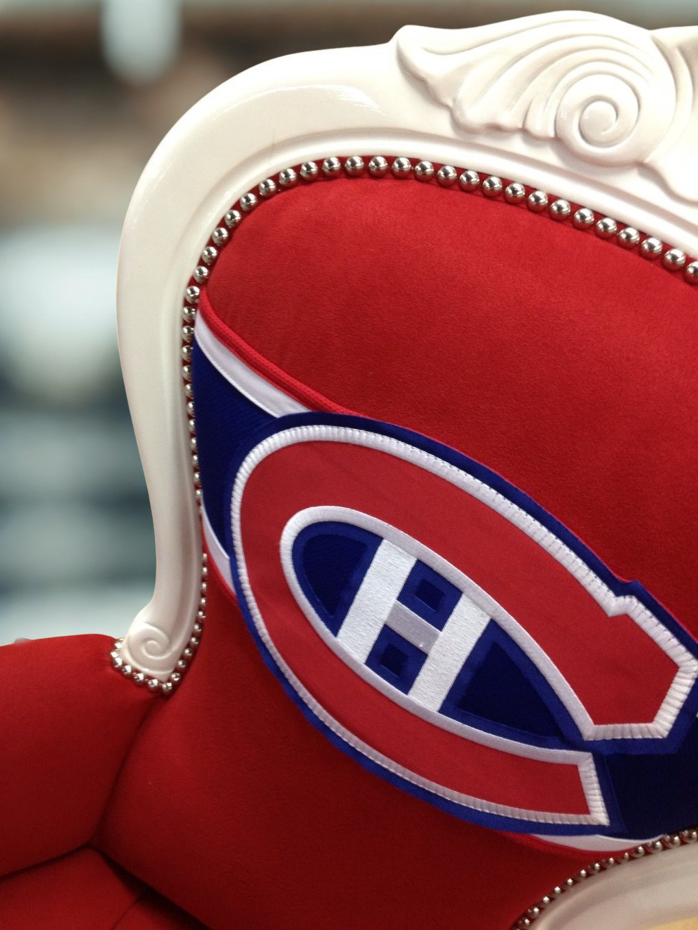 Close-up of a chair with red and blue sports team logo embroidery, white ornate wooden frame, and silver nailhead trim.