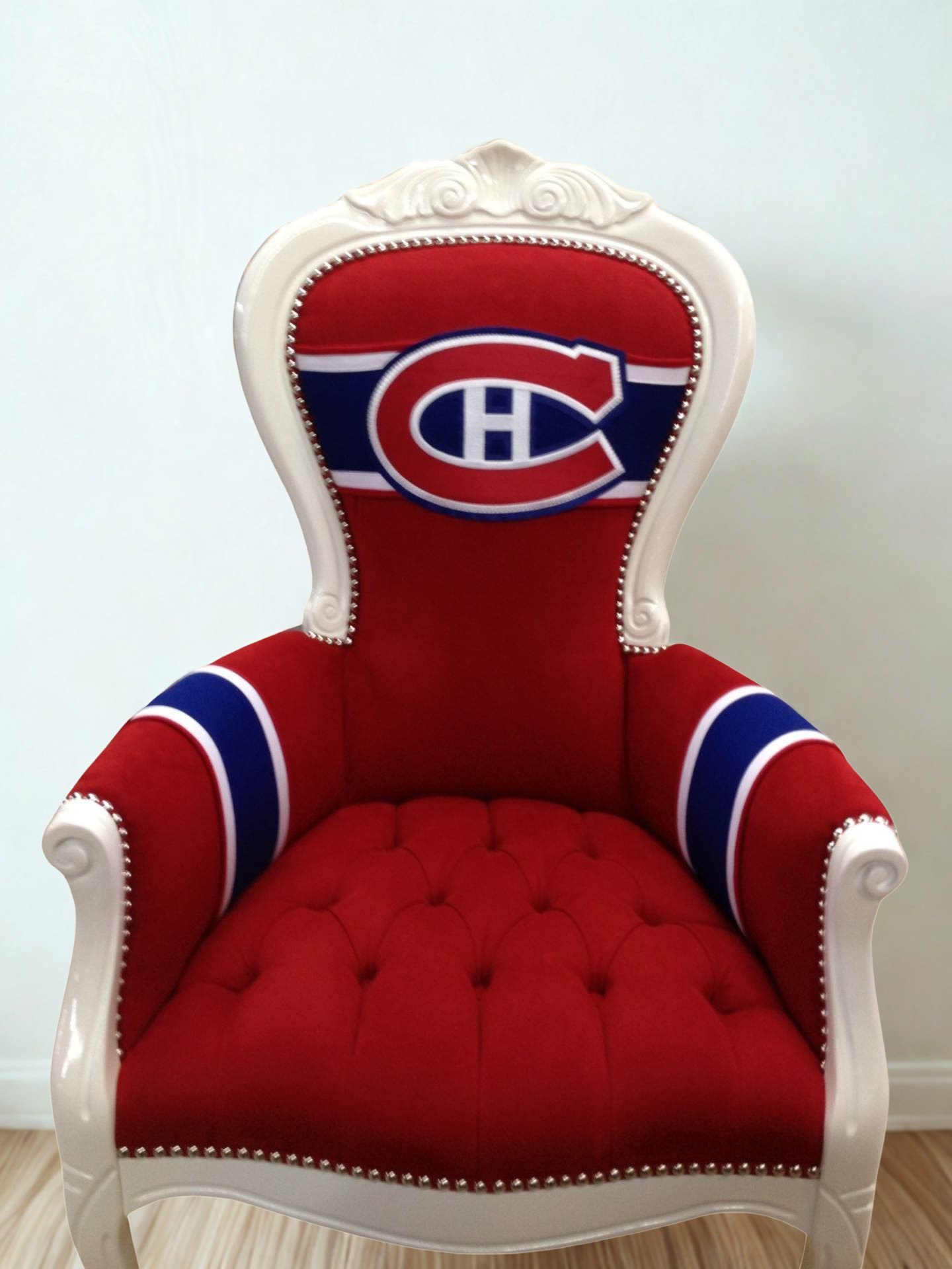 Red and white throne chair with Montreal Canadiens logo on the backrest, white carved wooden frame, red upholstery, and navy blue and white accents on the armrests, set on light wood flooring against a plain white wall.