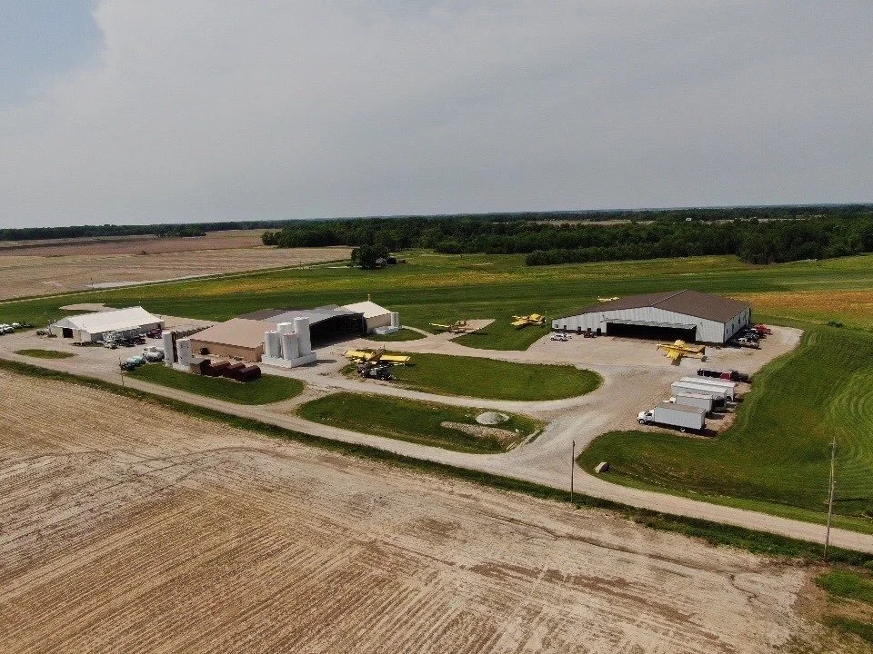 Aerial view of a farm with multiple large buildings, farm equipment, and trucks surrounded by fields and farmland.