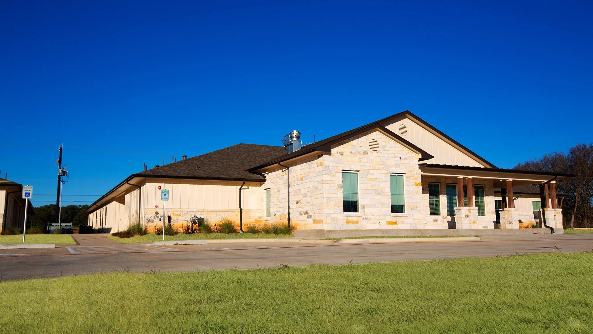 A modern building with a stone and siding exterior, sloped roof, and front porch supported by wooden columns, set against a clear blue sky.