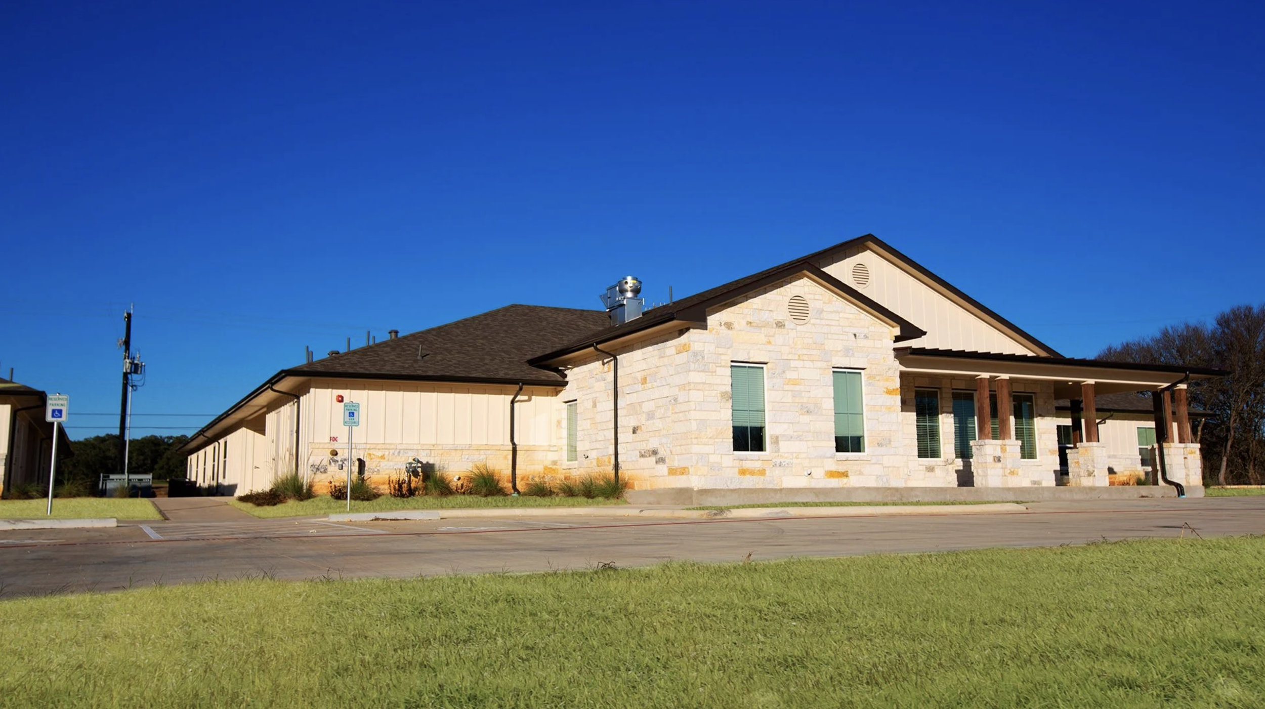 A modern building with a stone and siding exterior, sloped roof, and front porch supported by wooden columns, set against a clear blue sky.