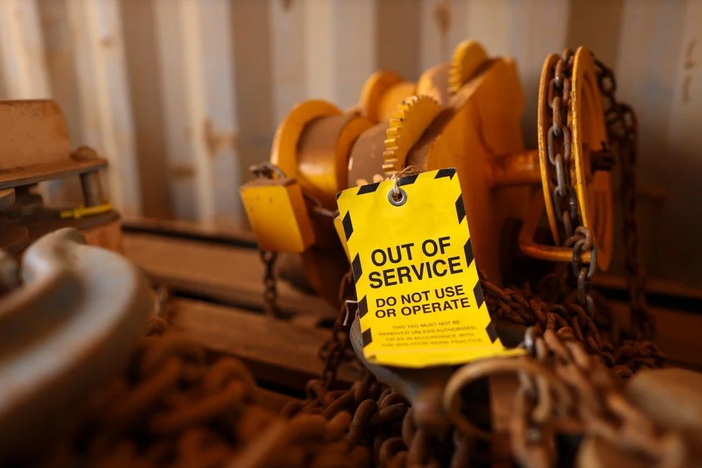 Close-up of industrial equipment with a yellow 'Out of Service' tag, caution chains, and rusted metal parts.
