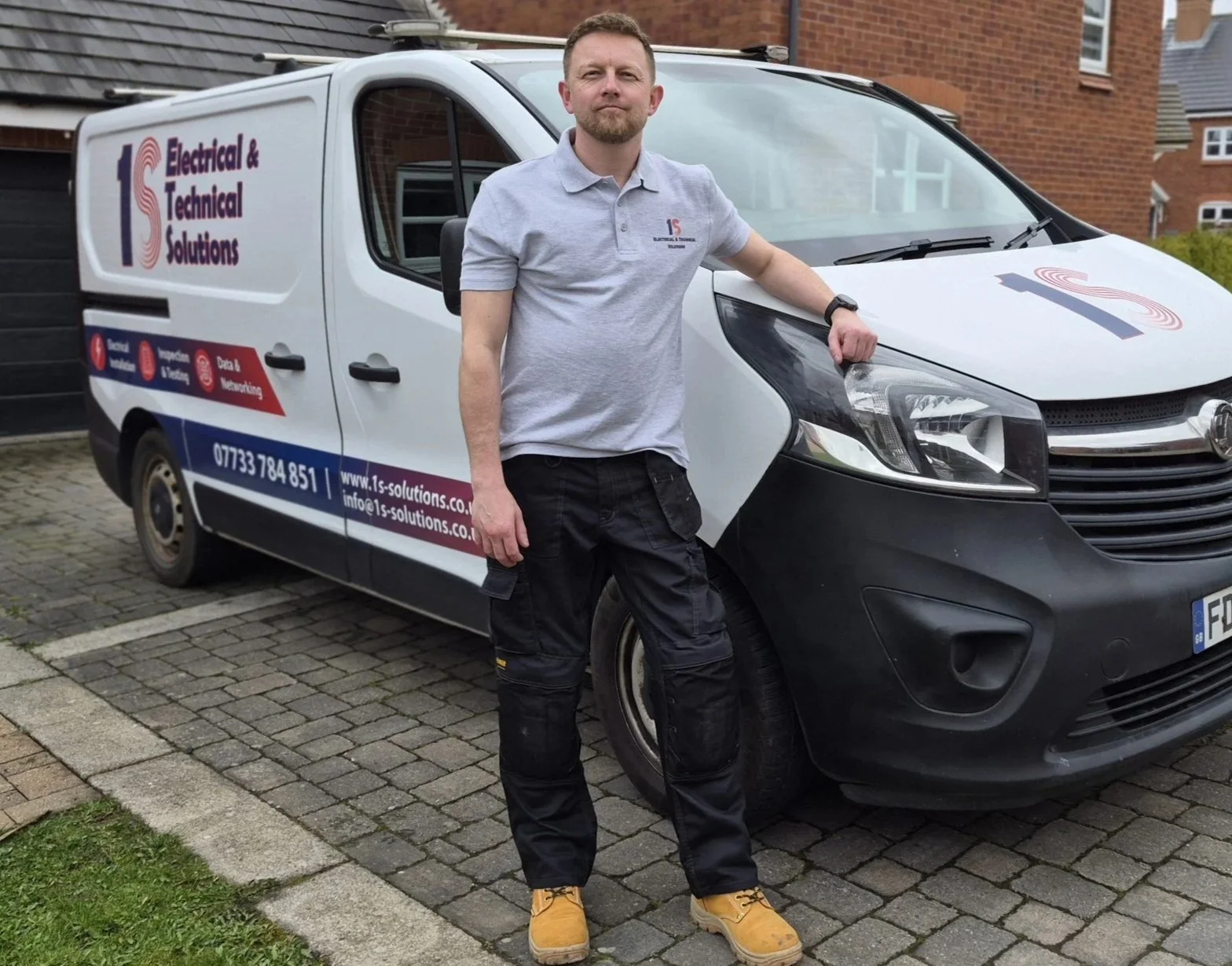 A man standing next to a company service van labeled 'Electrical & Technical Solutions' parked on a residential street.