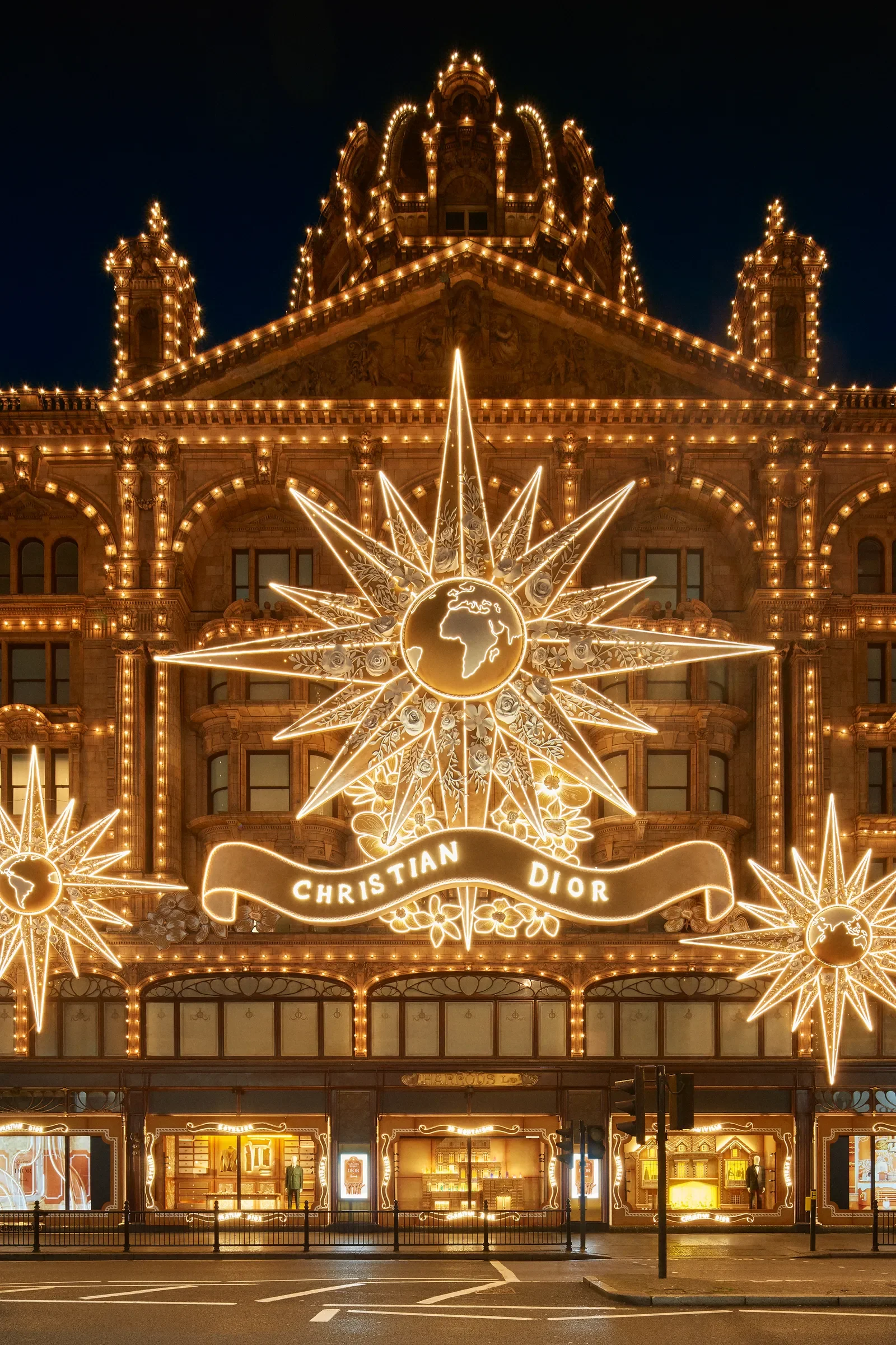 Illuminated Christmas storefront with ornate lighting, displaying the words 'Christian Dior' and decorative starburst designs in front of a historic building at night.