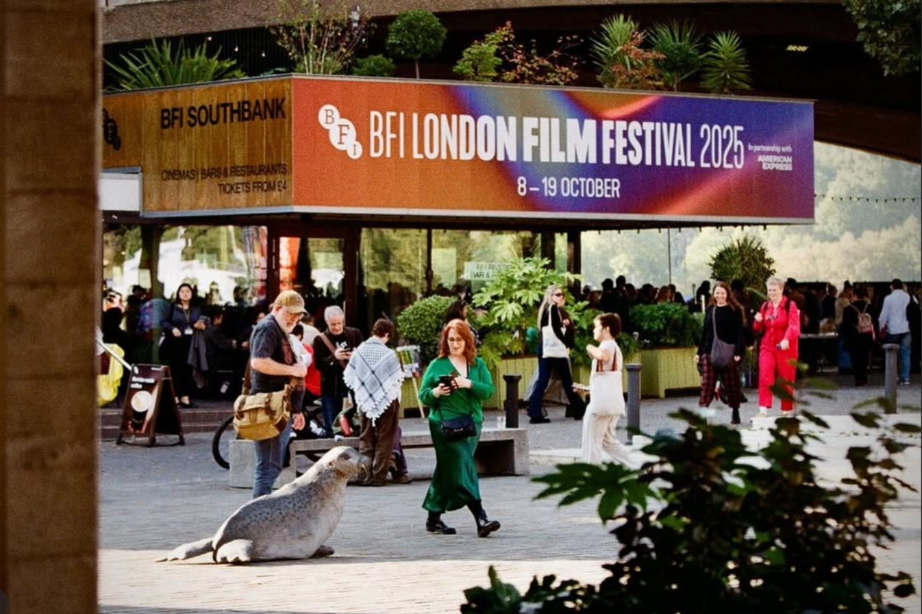 People walking outside at the entrance of BFI London Film Festival 2025, with a seal sculpture from Breena Farrelly Props and displays on the ground in the foreground. The festival banner is prominently displayed above.
