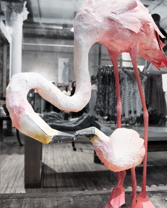 Artistic flamingo sculpture with pink and white body and long pink legs displayed in a store or gallery.
