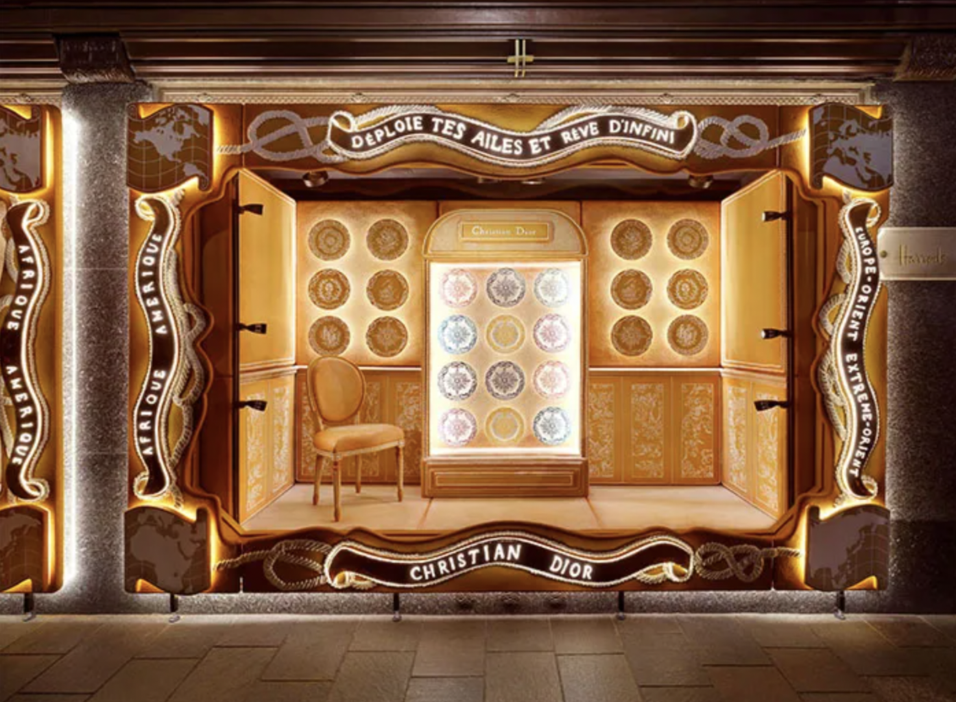 Display window featuring Christian Dior products with illuminated orange and gold decor, a chair, and decorative circular patterns on the back wall.