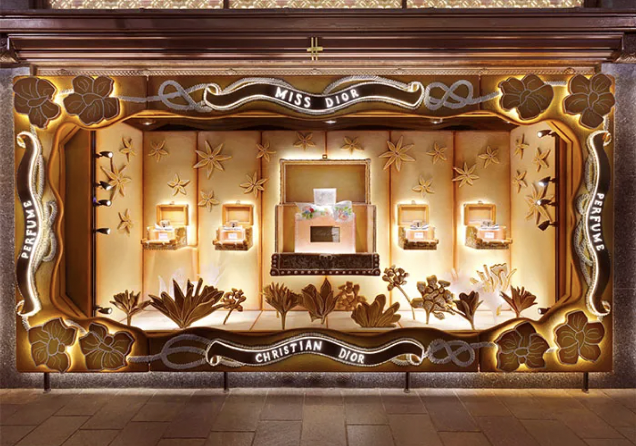 Decorative window display for Christian Dior's Miss Dior perfume with floral designs and illuminated boxes showcasing perfume bottles.