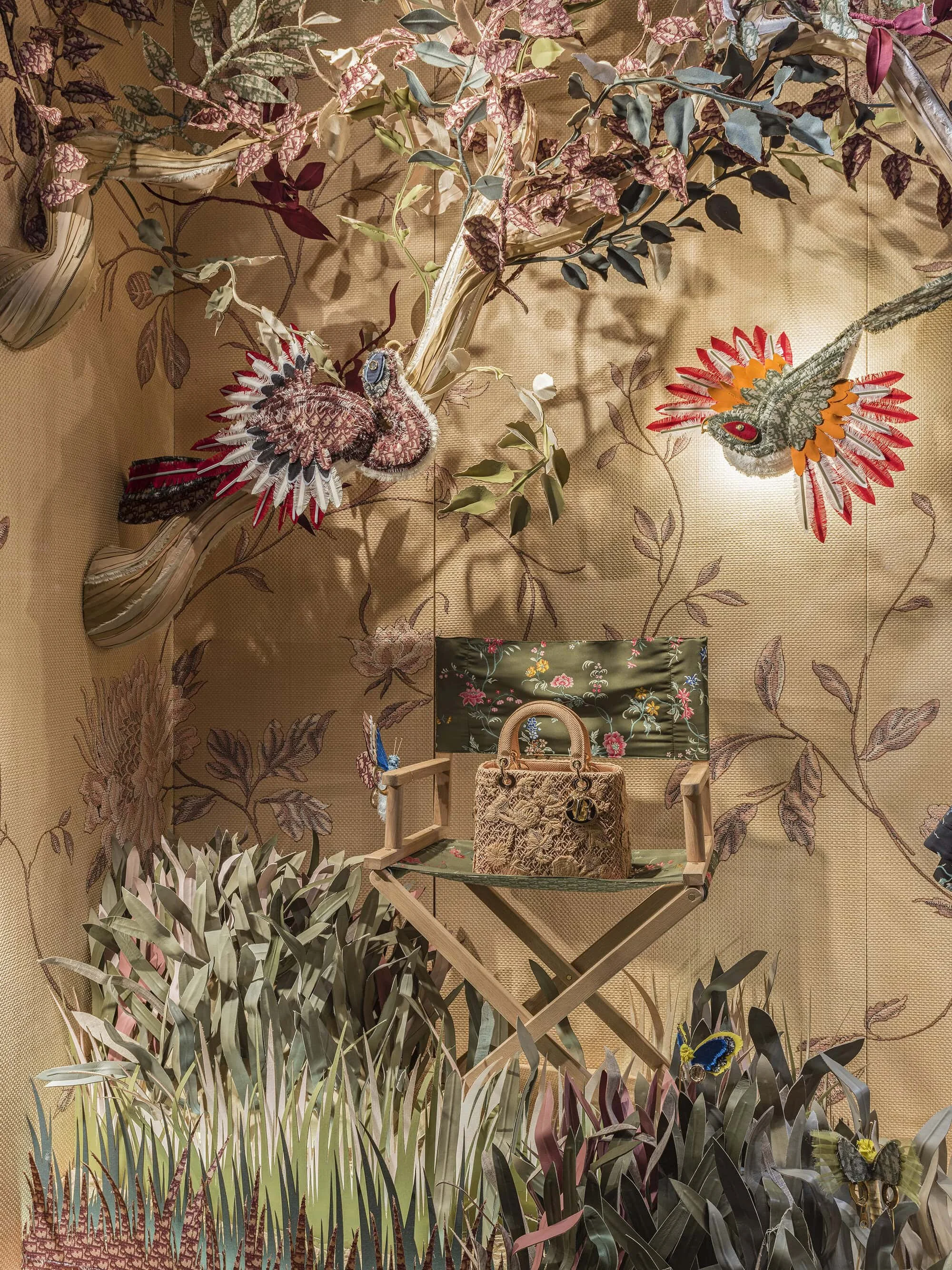 Display of a handbag on a decorated chair, surrounded by painted plants and butterflies on a floral wallpaper background in a fashion boutique.