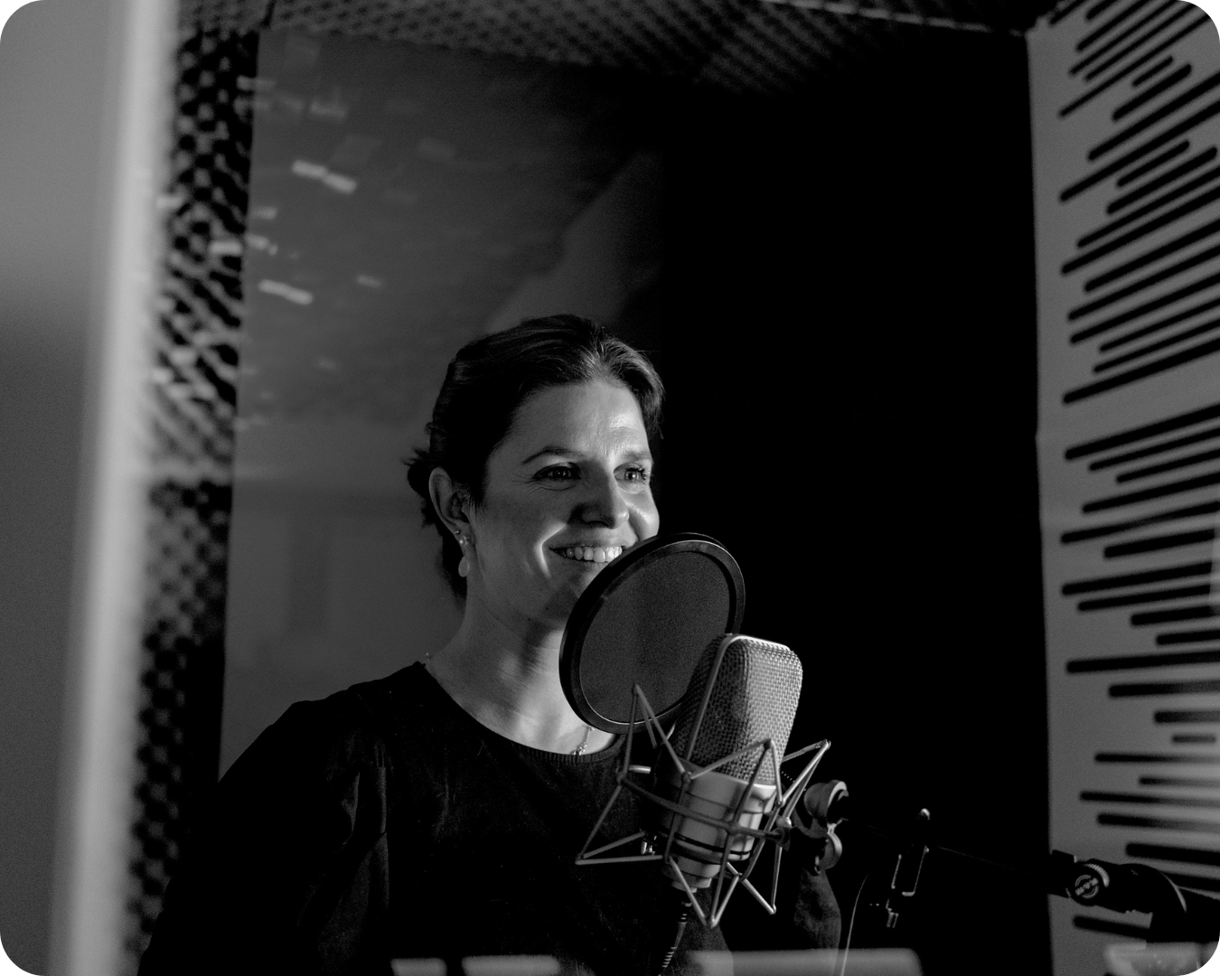 Eine lächelnde Frau steht vor einem Mikrofon in einem Tonstudio.