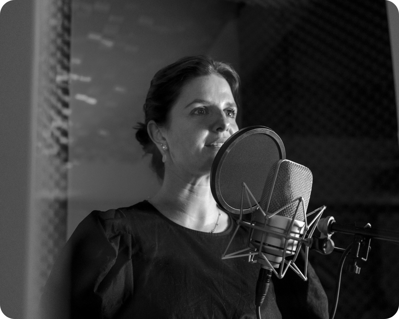 Schwarze und weiße Aufnahme einer Frau, die im Tonstudio vor einem Mikrofon singt oder spricht.