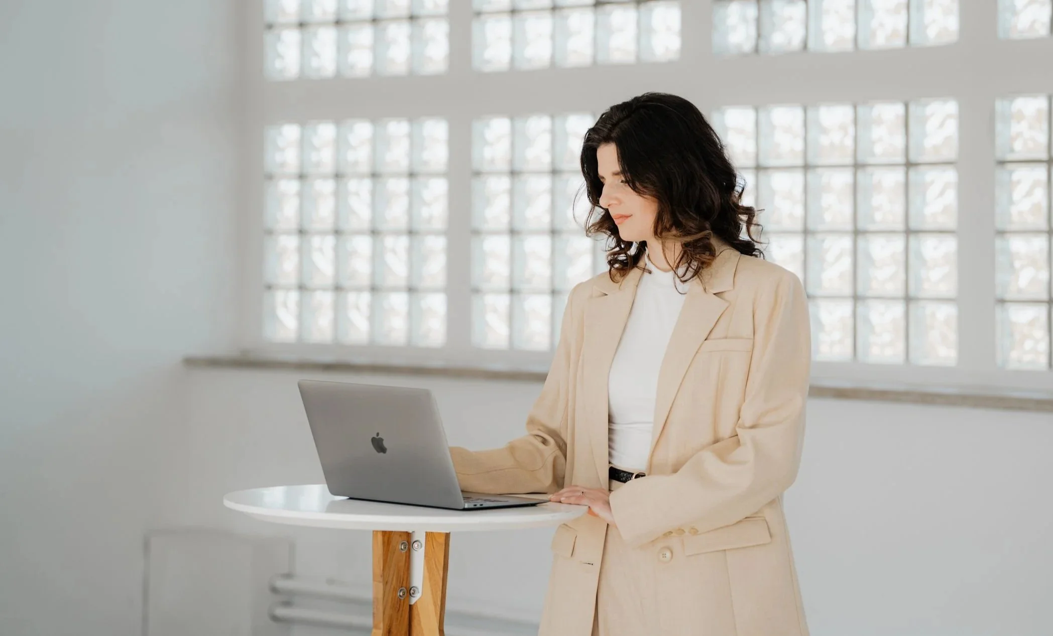 Frau arbeitet mit einem MacBook in einem hellen, modernen Raum mit großen Fenstern.