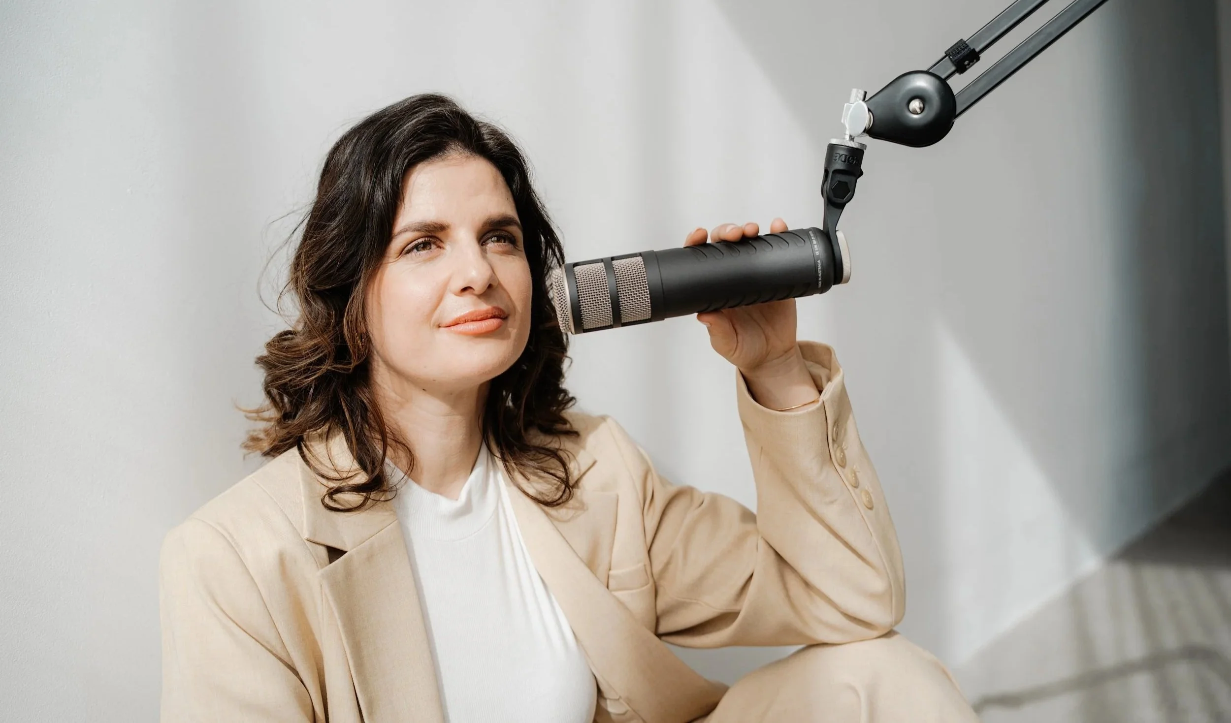 Eine Frau sitzt gegen eine Wand und spricht in ein Mikrofon, das an einer Armhalterung befestigt ist.