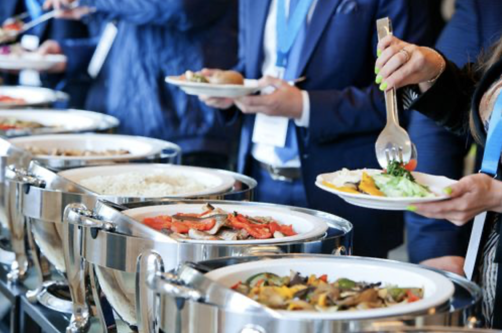 People serving themselves food from a buffet with various dishes on chafing dishes.