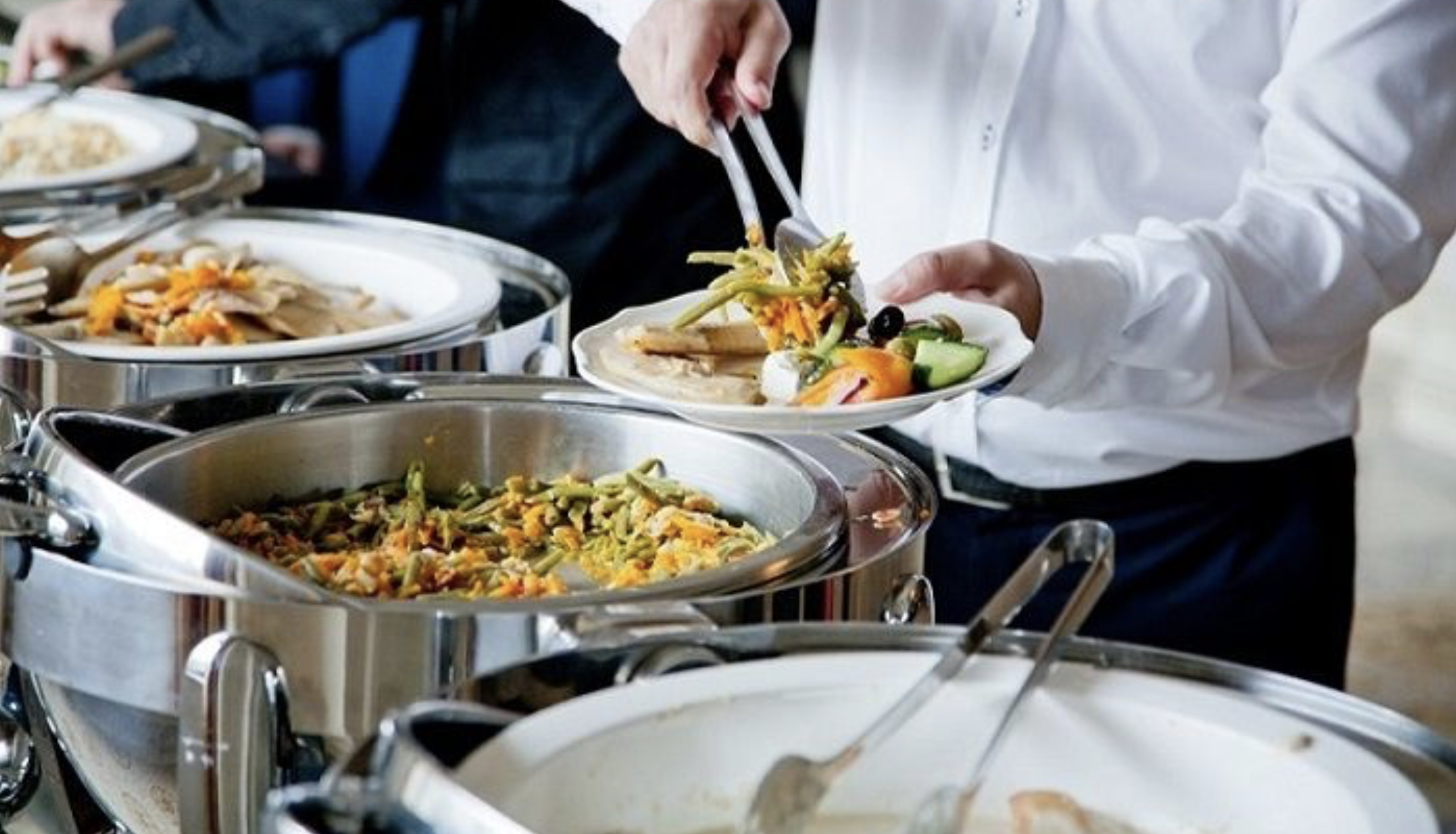 Person serving themselves food from a buffet with various hot and cold dishes.