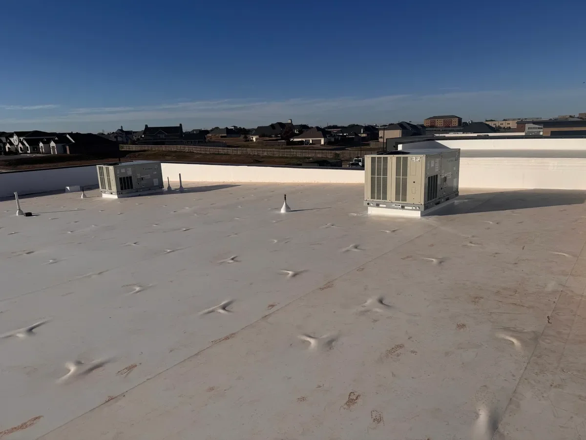 Rooftop with two HVAC units and white protective coating, with houses and a clear blue sky in the background.