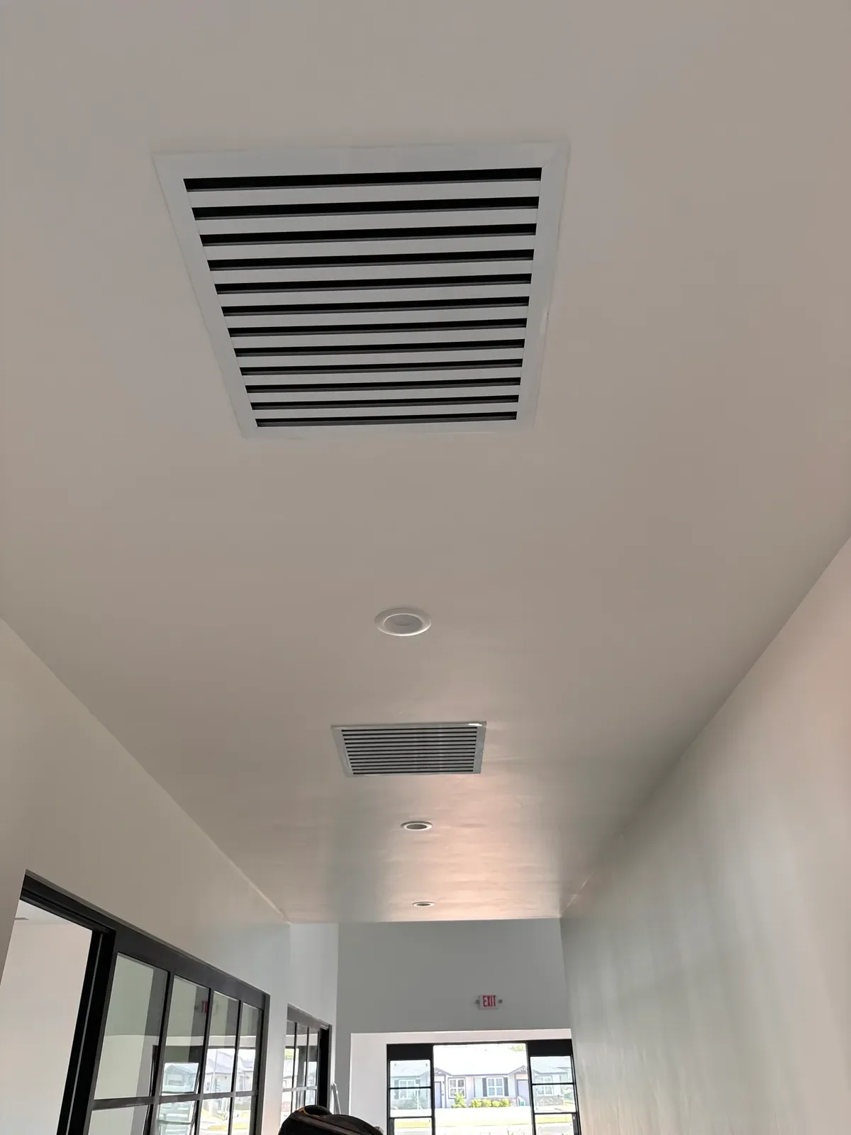 Ceiling with multiple ventilation vents and recessed lighting fixtures in a modern interior space, with large glass doors at the end of the hallway.