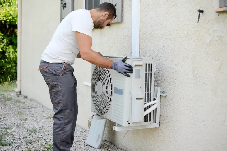 A man repairing an outdoor air conditioning unit on the side of a house.