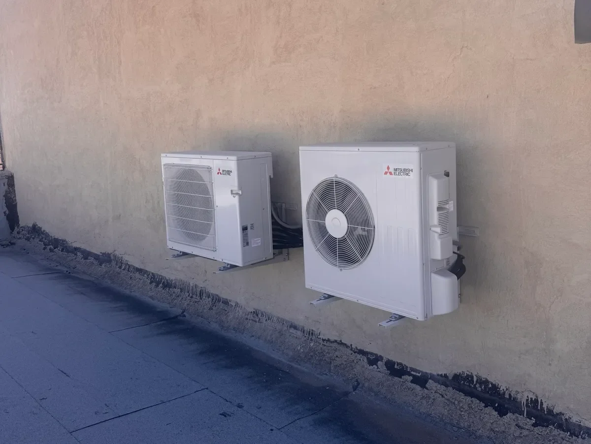 Two outdoor Mitsubishi Electric air conditioning units mounted on a beige wall.