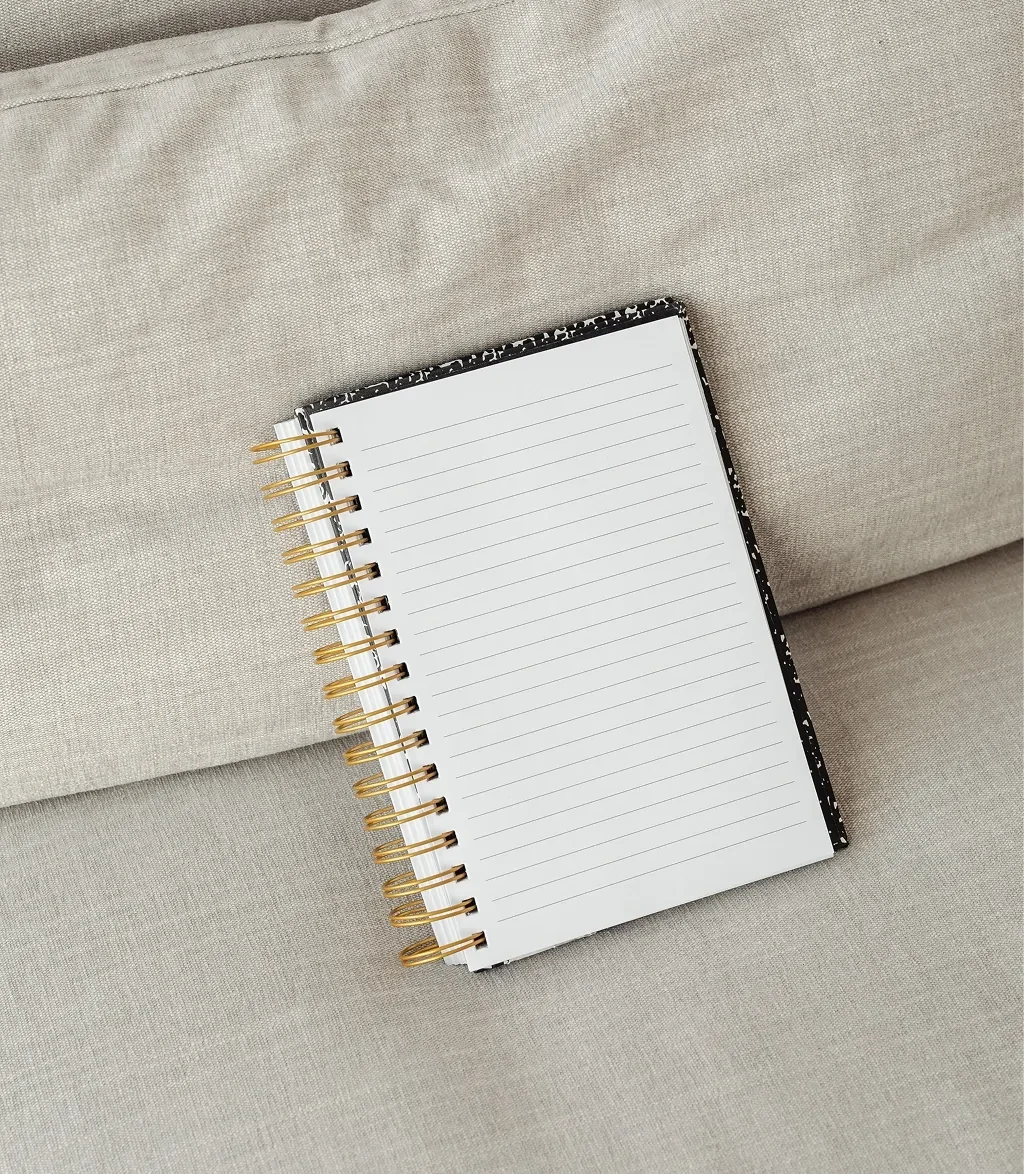 Un carnet à pages blanches avec lignes, placé sur un canapé en tissu beige clair.