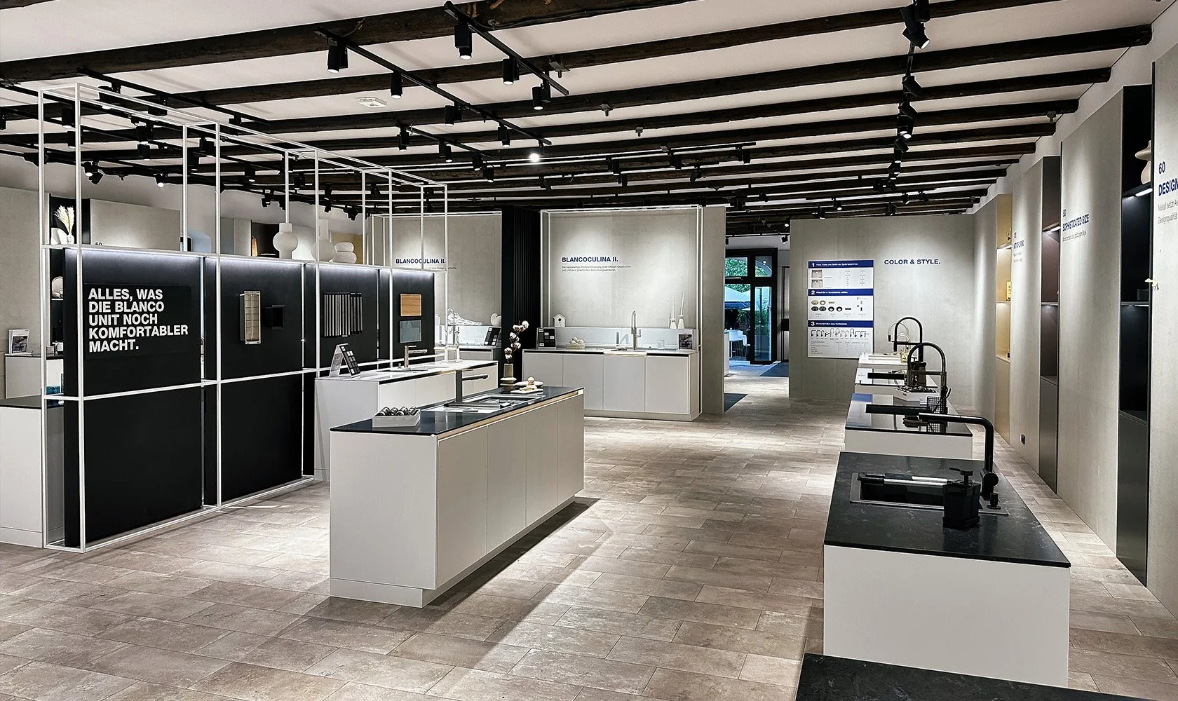 Interior of a modern showroom displaying kitchen fixtures and appliances with white and black cabinetry and fixtures, illuminated by track lighting.