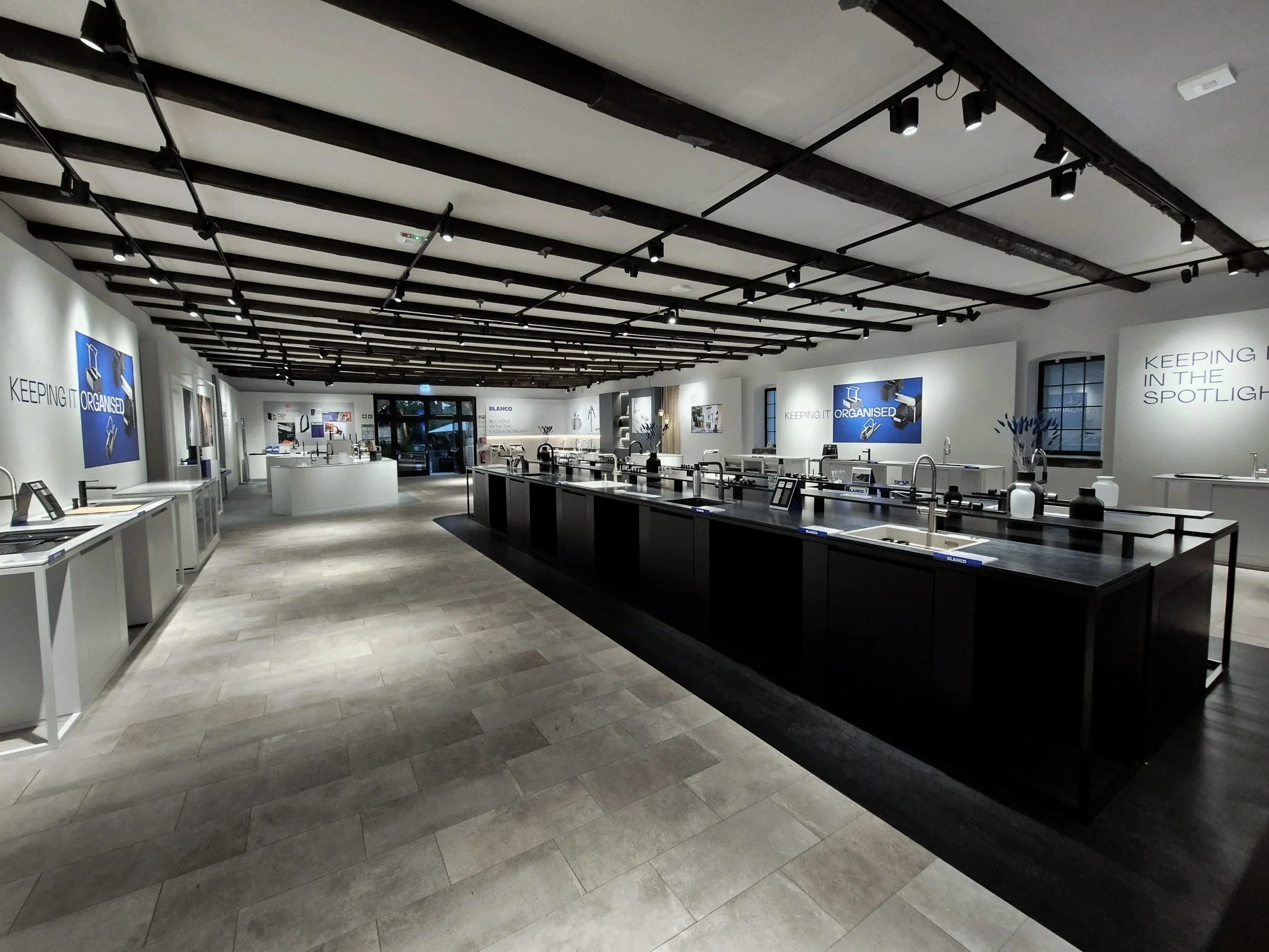 Interior of a modern kitchenware store with display counters, shelves, and wall-mounted screens, featuring a sleek, minimalist design with black and white decor.