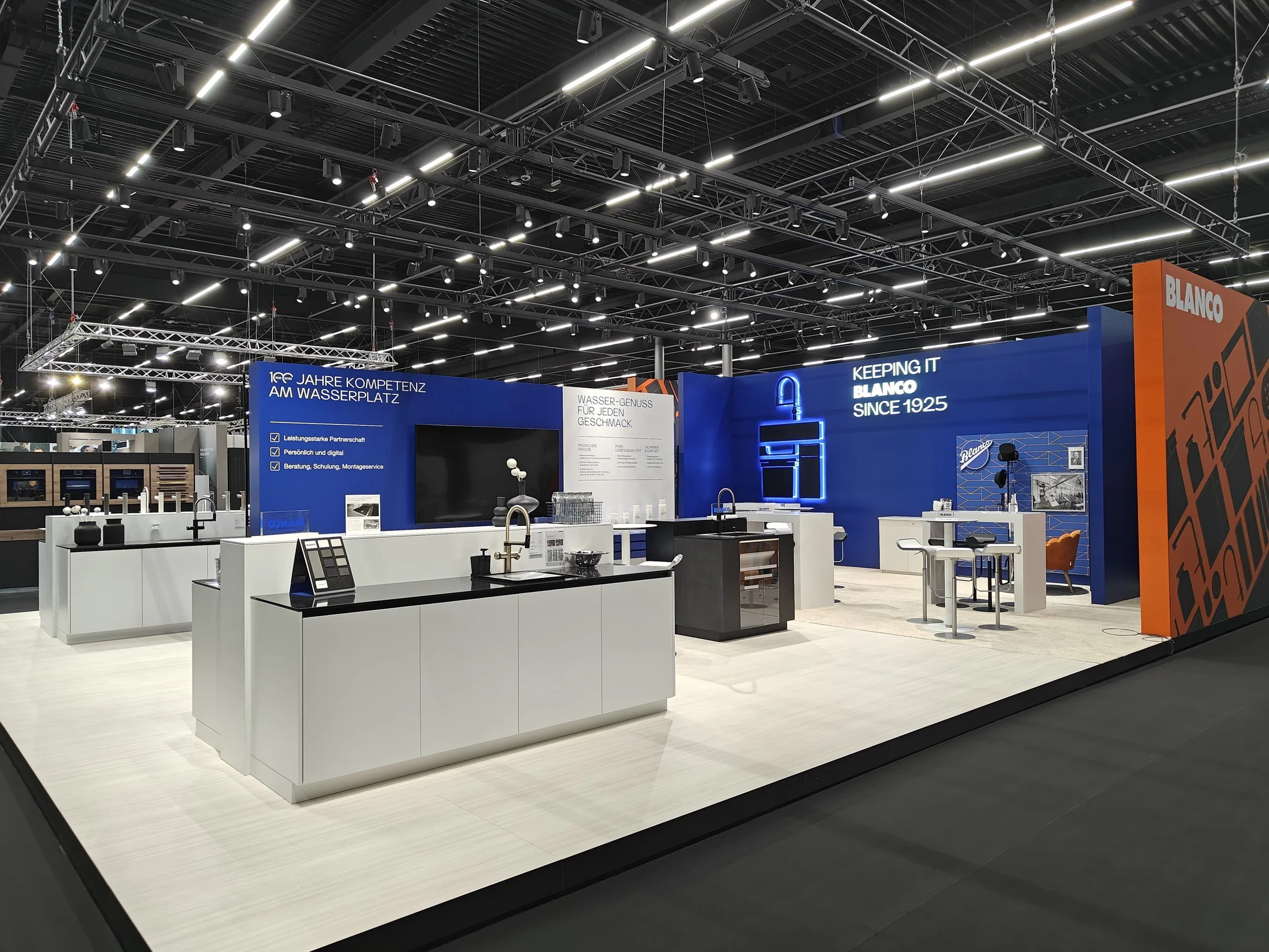 Exhibition booth with kitchen fixtures, faucet displays, and signage highlighting water expertise, with blue and orange branding elements.