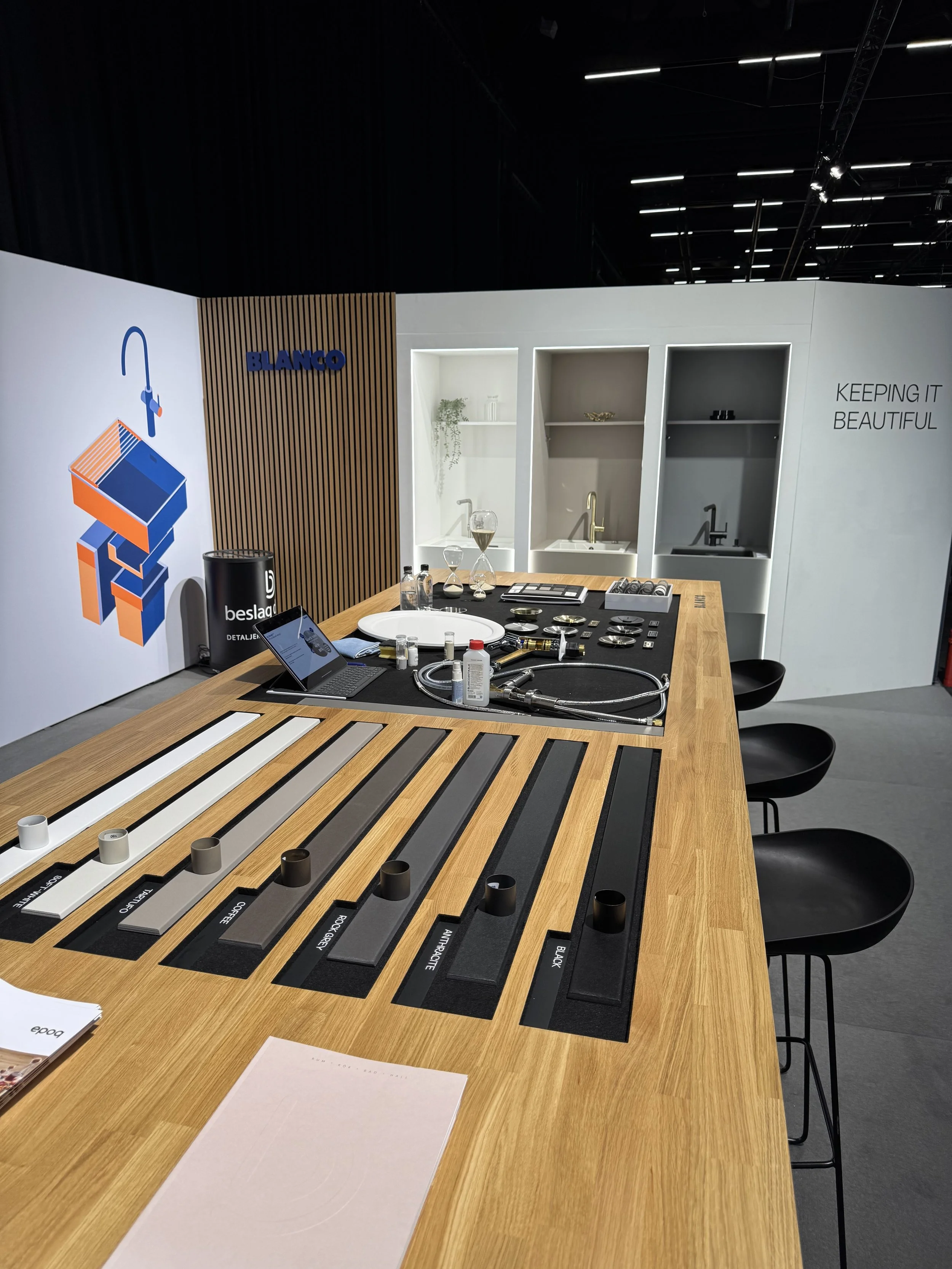 Showroom display with color and material samples on a wooden table, kitchen fixtures on the wall, and a promotional wall with the words "Keeping it Beautiful".